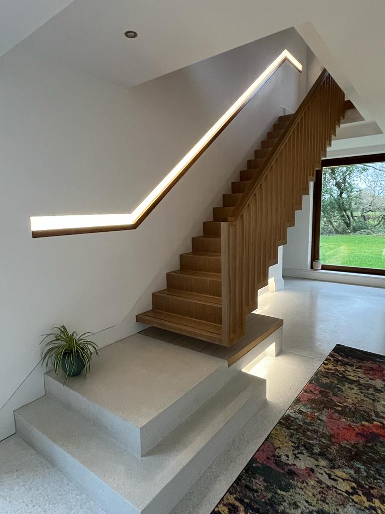 Modern wooden staircase with integrated LED handrail lighting.